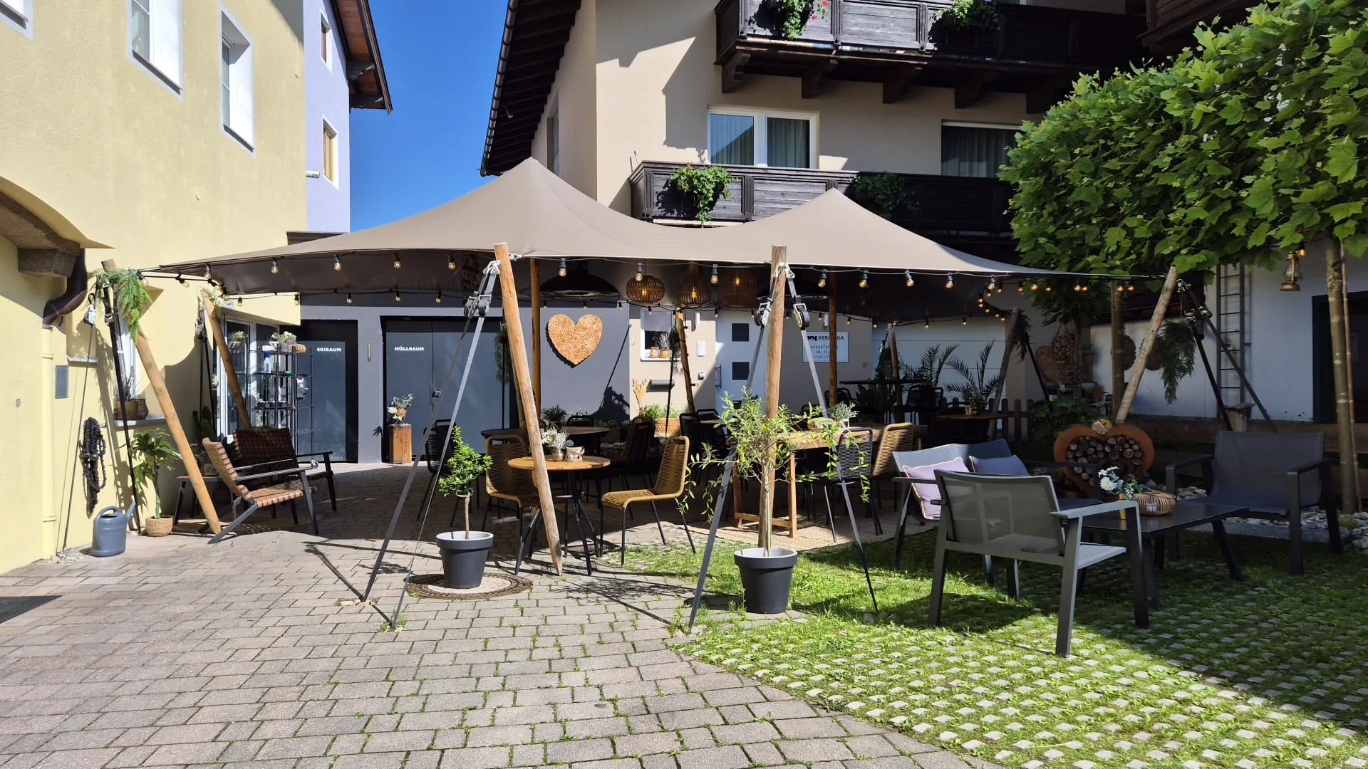 Gemütlicher Außenbereich eines Cafés mit befestigtem Sonnensegel und Pflanzen.